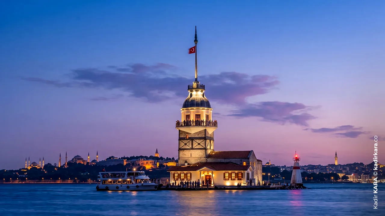 Mavi saatte ışıklandırılmış Kız Kulesi'nin lacivert gökyüzü önündeki görünümü
